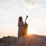 female-musician-with-cello-outdoors-sunset_23-2148737116